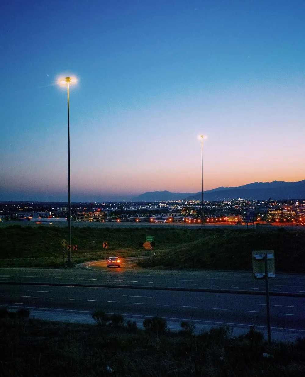 Street lights over a highway at blue hour, with city lights and mountains on the horizon